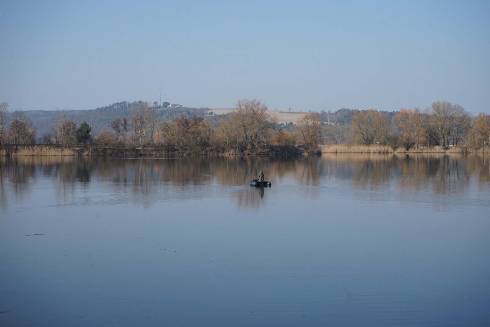 Ruhiger Baggersee im Herbst, Schilf und kahle Bäume am Ufer