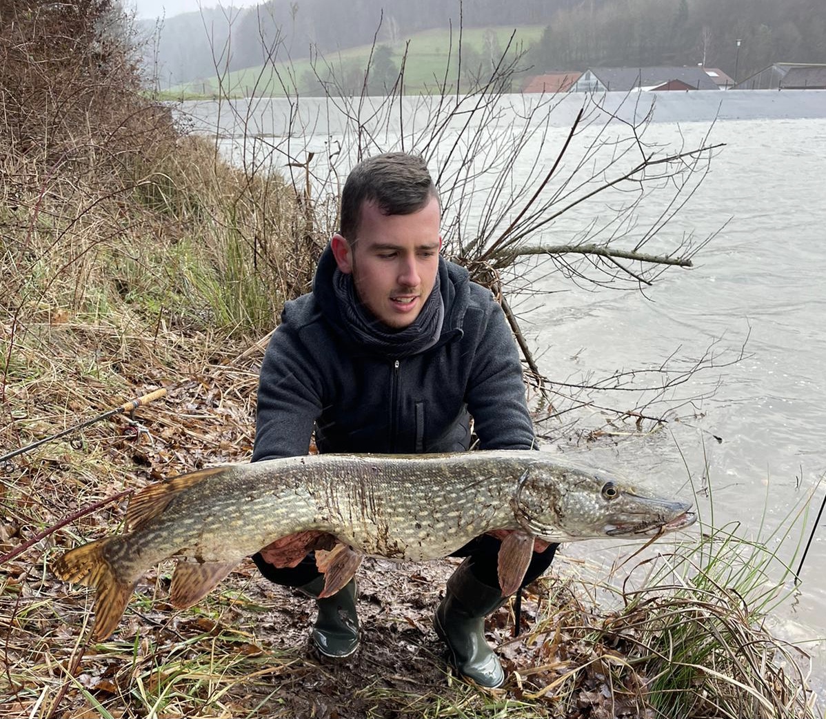 Angler mit einem kapitalen Hecht am Ufer im Spätherbst