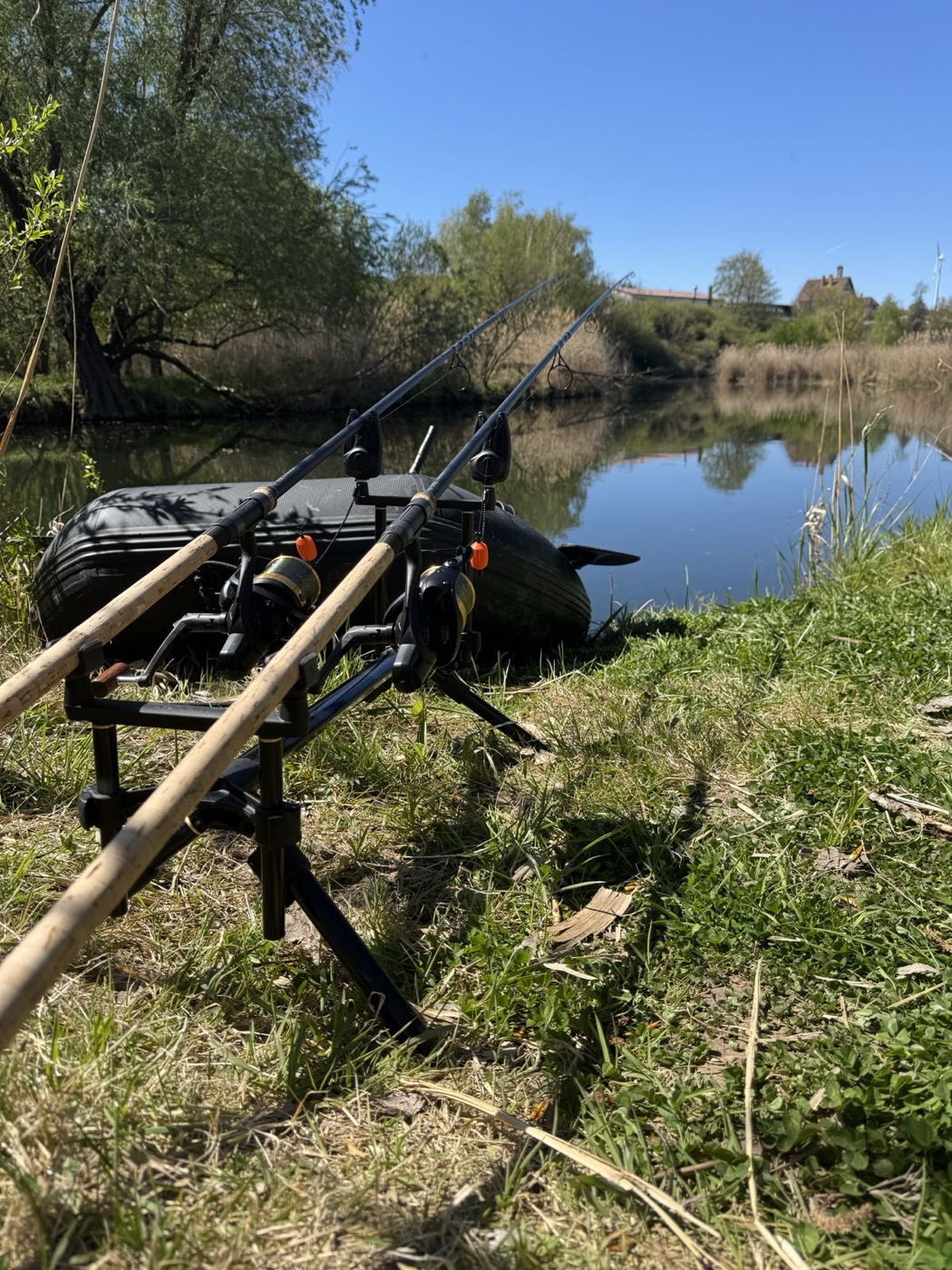 Nahaufnahme eines Rod Pods mit zwei Ruten am Ufer, dahinter das Schlauchboot